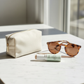 CC Cream stick on marble beside sunglasses and a makeup pouch